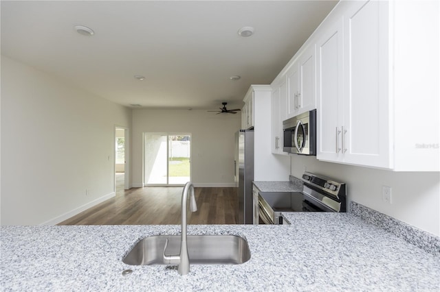 kitchen with light stone counters, appliances with stainless steel finishes, sink, white cabinets, and dark wood-type flooring