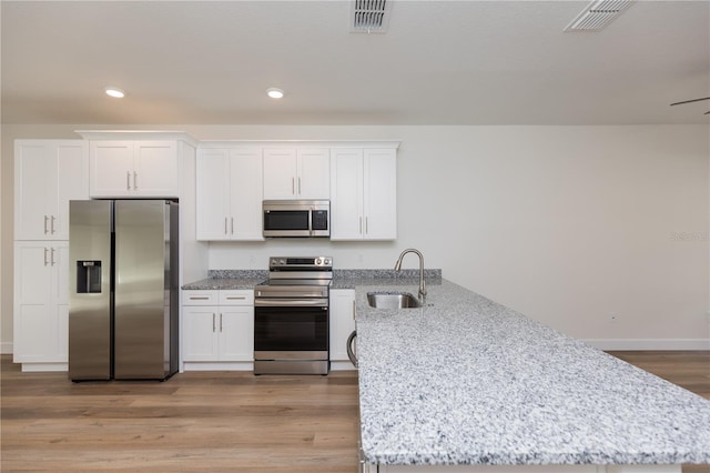 kitchen with stainless steel appliances, white cabinetry, sink, and light stone counters