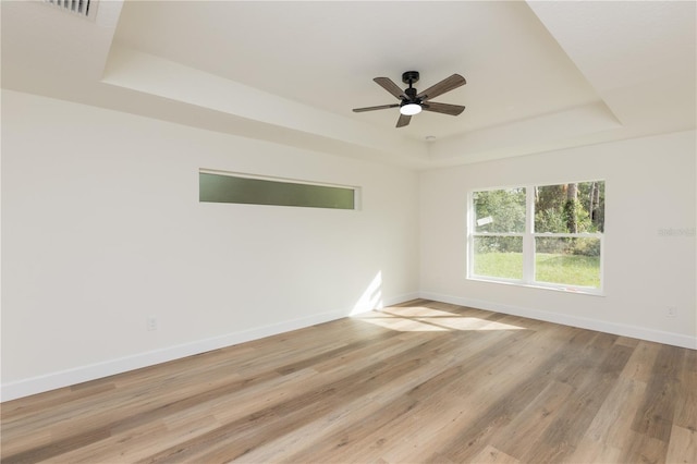 unfurnished room with ceiling fan, a tray ceiling, and light hardwood / wood-style floors