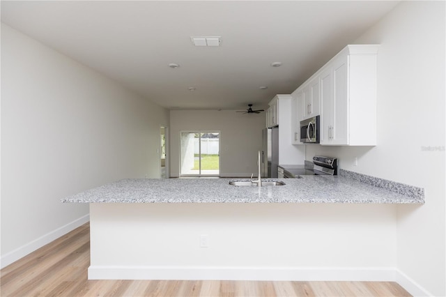 kitchen featuring light hardwood / wood-style floors, kitchen peninsula, appliances with stainless steel finishes, light stone countertops, and white cabinets