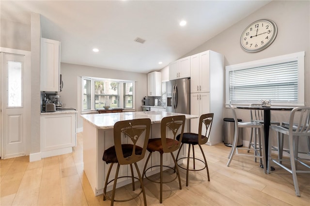 kitchen featuring stainless steel fridge with ice dispenser, white cabinetry, a breakfast bar, and vaulted ceiling