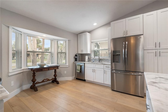 kitchen featuring white cabinets, appliances with stainless steel finishes, vaulted ceiling, and light hardwood / wood-style flooring