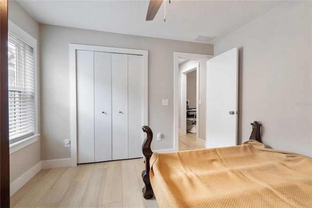 bedroom with a textured ceiling, a closet, ceiling fan, and light wood-type flooring