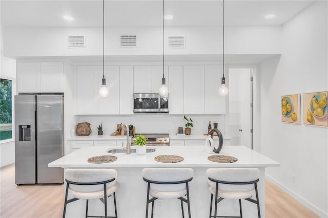 kitchen featuring an island with sink, stainless steel appliances, white cabinets, and hanging light fixtures