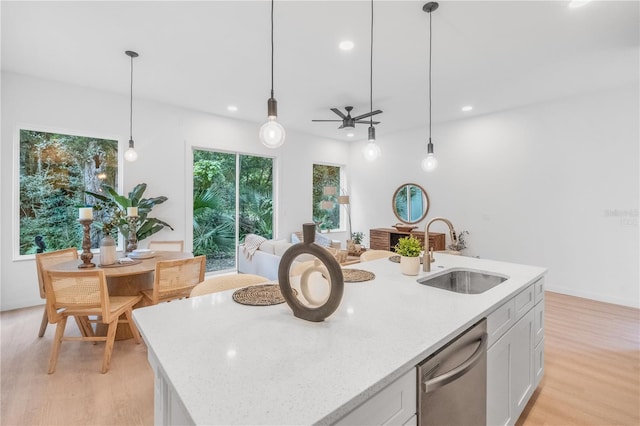 kitchen featuring hanging light fixtures, white cabinetry, light wood-type flooring, stainless steel dishwasher, and sink