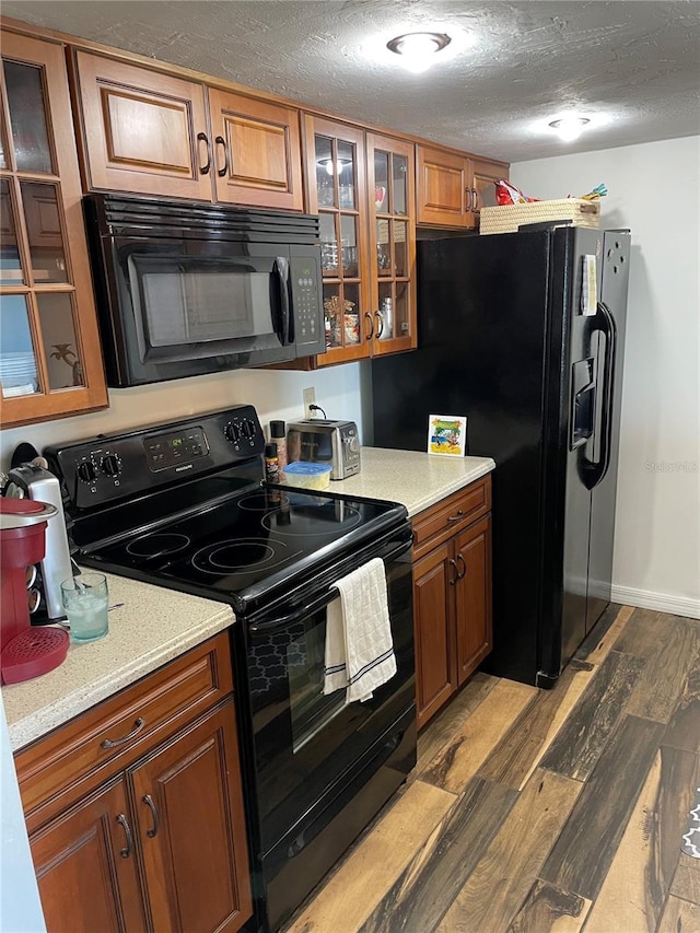 kitchen featuring a textured ceiling, black appliances, and dark hardwood / wood-style flooring