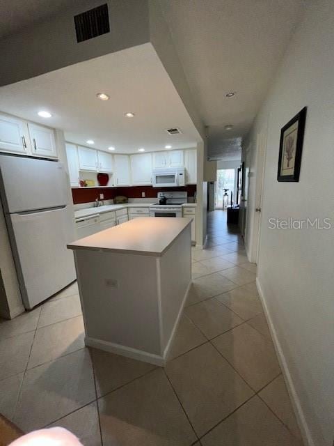 kitchen with white cabinetry, a kitchen island, white appliances, and light tile patterned floors