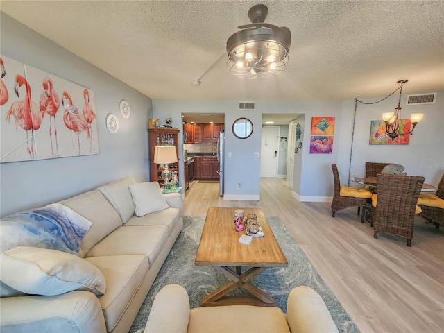 living room featuring a textured ceiling, a chandelier, and light wood-type flooring