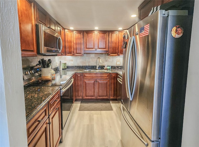 kitchen with dark stone counters, tasteful backsplash, light hardwood / wood-style flooring, appliances with stainless steel finishes, and sink