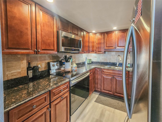 kitchen with backsplash, sink, light wood-type flooring, stainless steel appliances, and dark stone counters