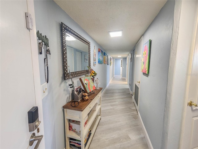 hall with a textured ceiling and light hardwood / wood-style flooring