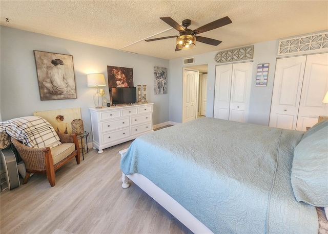 bedroom featuring two closets, a textured ceiling, ceiling fan, and light hardwood / wood-style flooring