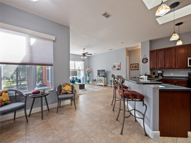 kitchen featuring a breakfast bar, a skylight, ceiling fan, and light tile flooring