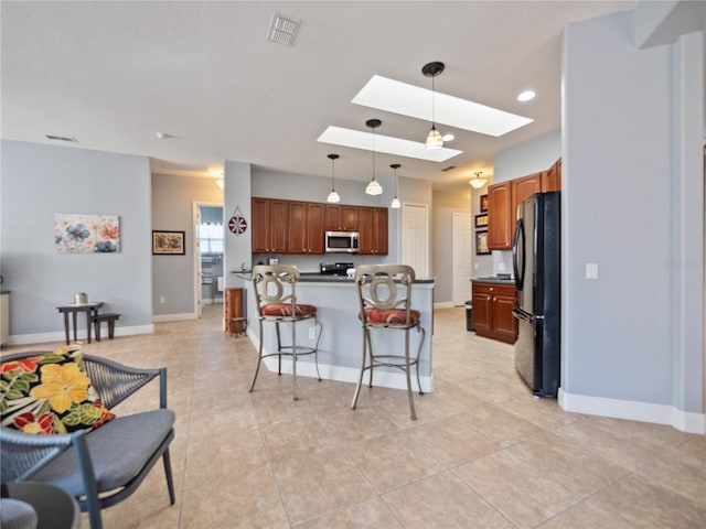 kitchen with black refrigerator, hanging light fixtures, a skylight, a breakfast bar area, and light tile flooring