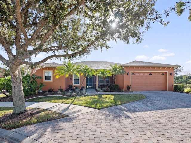 single story home with a front lawn, decorative driveway, an attached garage, and stucco siding