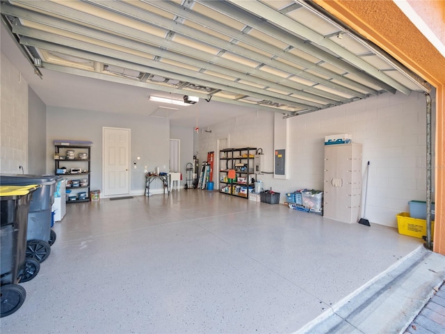 garage featuring concrete block wall, electric panel, and a garage door opener