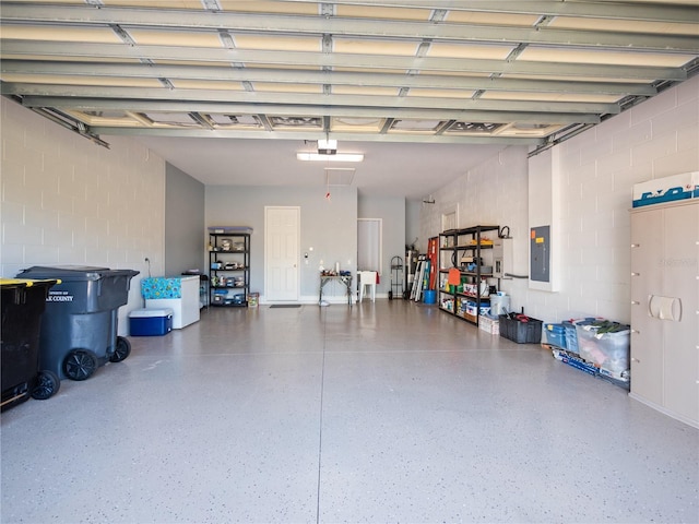 garage featuring a garage door opener, concrete block wall, and electric panel