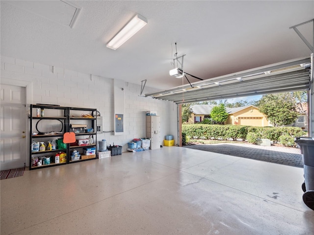 garage with concrete block wall, electric panel, and a garage door opener