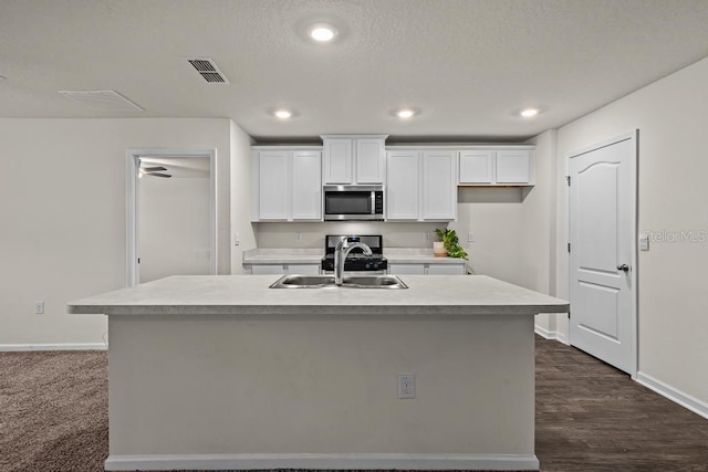 kitchen featuring dark hardwood / wood-style floors, appliances with stainless steel finishes, sink, an island with sink, and white cabinets