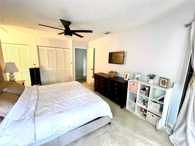 carpeted bedroom featuring a ceiling fan, visible vents, and two closets