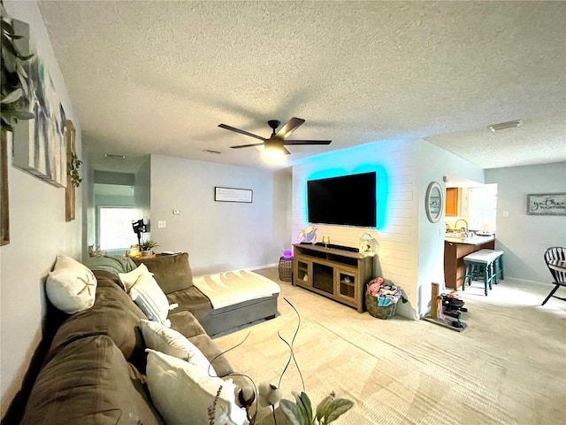 living area with light carpet, ceiling fan, a textured ceiling, and baseboards