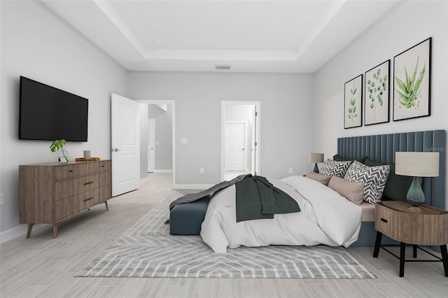 bedroom with light wood-type flooring, visible vents, a raised ceiling, ensuite bathroom, and baseboards