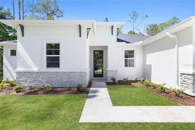 view of front facade featuring a front yard, stone siding, and stucco siding