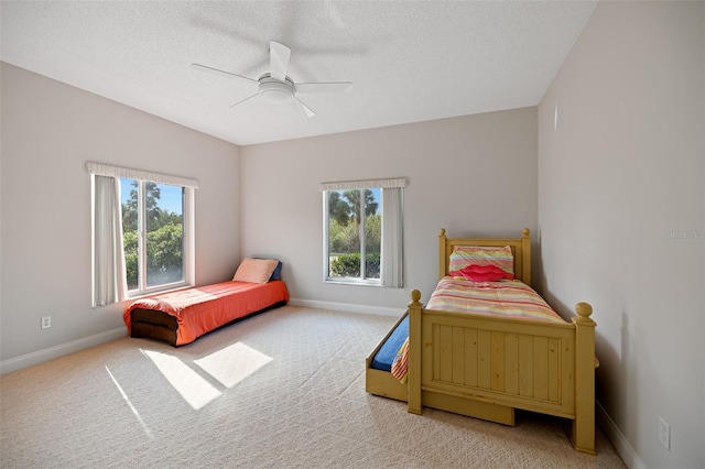 carpeted bedroom with a textured ceiling, ceiling fan, and multiple windows