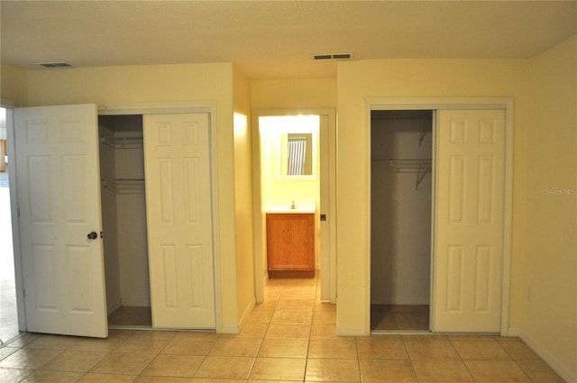 unfurnished bedroom with light tile floors, sink, and two closets