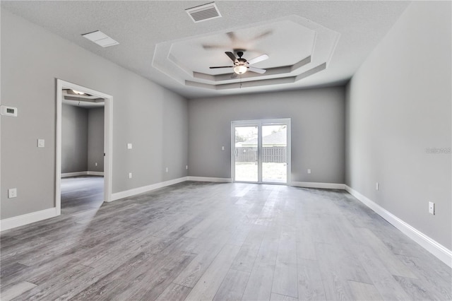 spare room featuring a textured ceiling, a tray ceiling, ceiling fan, and light wood-type flooring