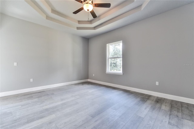 spare room featuring a raised ceiling, ceiling fan, and light wood-type flooring