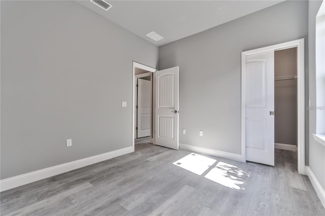 unfurnished bedroom featuring a walk in closet, a closet, and light wood-type flooring