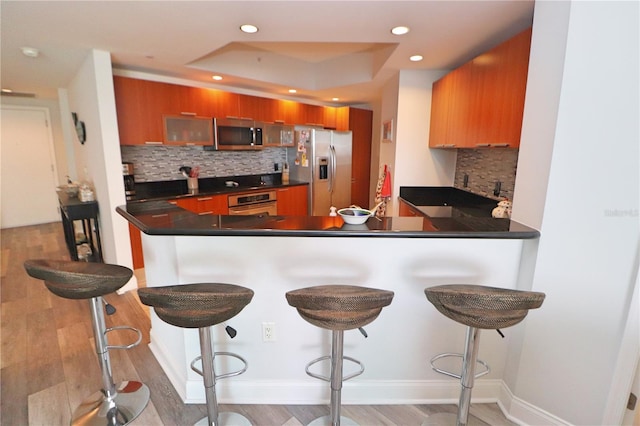 kitchen featuring a kitchen bar, light hardwood / wood-style floors, stainless steel appliances, a raised ceiling, and tasteful backsplash