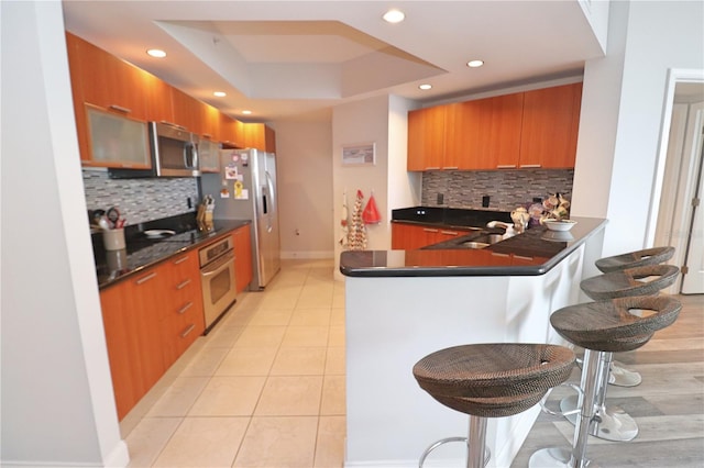 kitchen with stainless steel appliances, light tile floors, a raised ceiling, tasteful backsplash, and a breakfast bar area