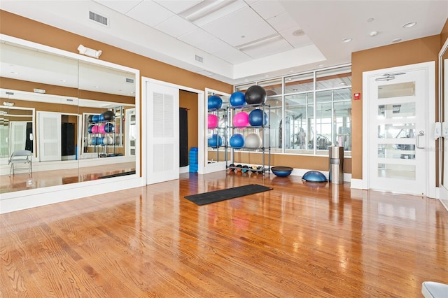 workout room with a raised ceiling and light hardwood / wood-style flooring