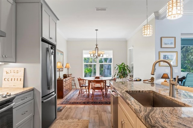 kitchen with light stone countertops, appliances with stainless steel finishes, sink, a chandelier, and pendant lighting