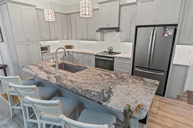 kitchen featuring a breakfast bar, light hardwood / wood-style floors, stainless steel refrigerator, electric range oven, and pendant lighting