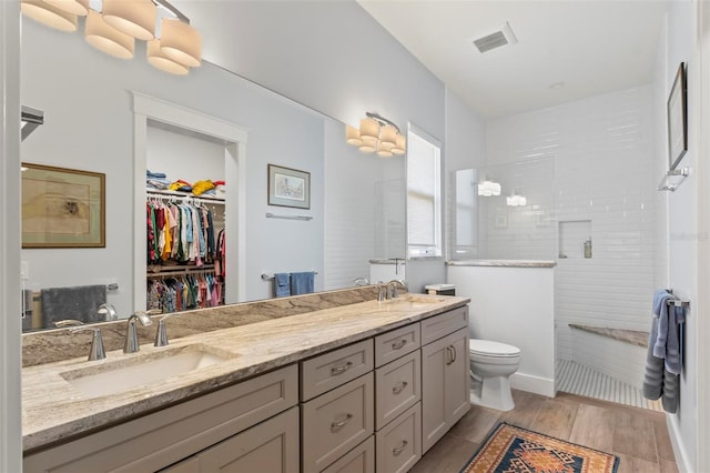 bathroom with double vanity, toilet, tiled shower, and hardwood / wood-style flooring