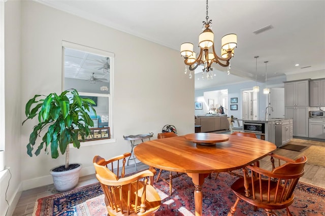 dining room with a notable chandelier, crown molding, sink, and light wood-type flooring