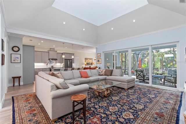 living room featuring a towering ceiling, ornamental molding, and light hardwood / wood-style flooring