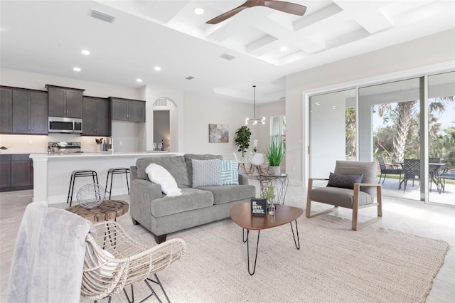 living room featuring beam ceiling, coffered ceiling, ceiling fan with notable chandelier, and light tile floors