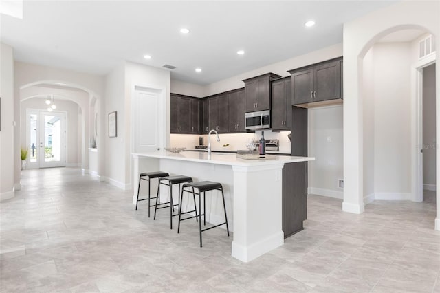 kitchen with light tile floors, french doors, a breakfast bar area, dark brown cabinetry, and sink