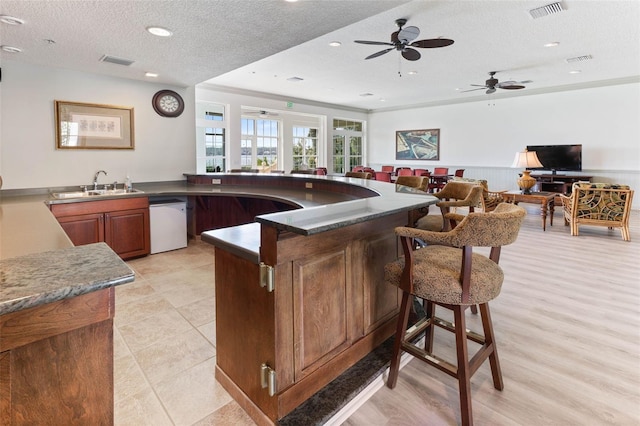 kitchen with ceiling fan, sink, a kitchen breakfast bar, dishwasher, and a textured ceiling