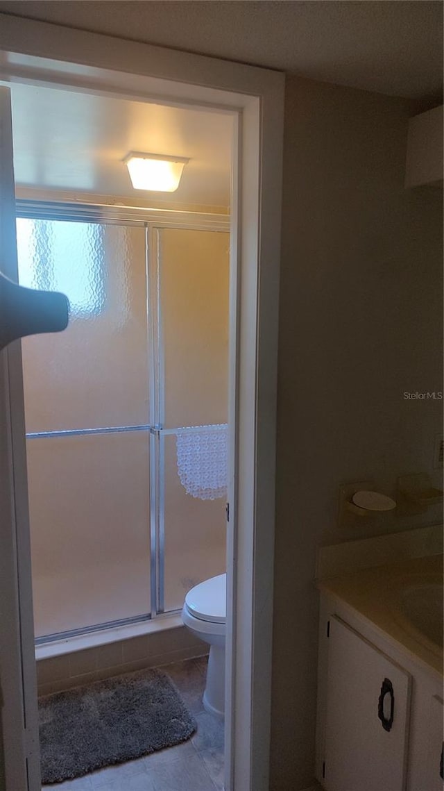 bathroom with toilet, tile floors, an enclosed shower, and vanity