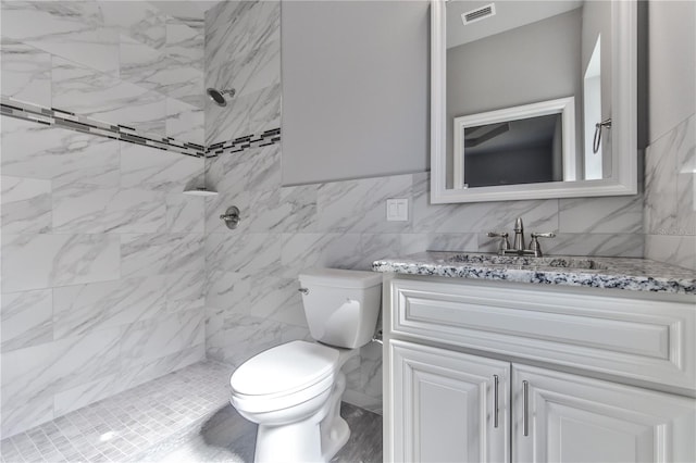 bathroom with tile walls, toilet, vanity, and tiled shower