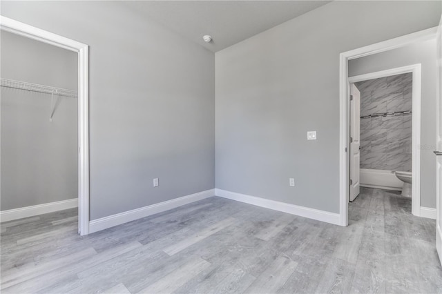 unfurnished bedroom featuring ensuite bathroom, a closet, and light wood-type flooring