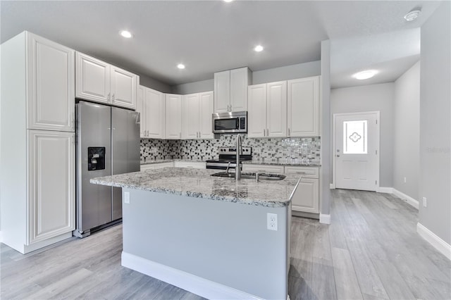 kitchen with light hardwood / wood-style floors, a kitchen island with sink, white cabinets, and appliances with stainless steel finishes