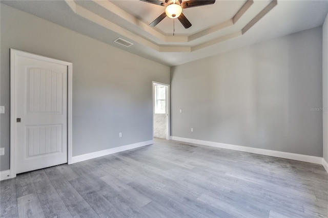 unfurnished room with light hardwood / wood-style flooring, a tray ceiling, and ceiling fan