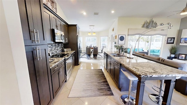 kitchen with an island with sink, light stone counters, backsplash, a breakfast bar area, and stainless steel appliances