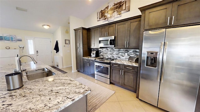 kitchen with tasteful backsplash, light stone counters, appliances with stainless steel finishes, and sink